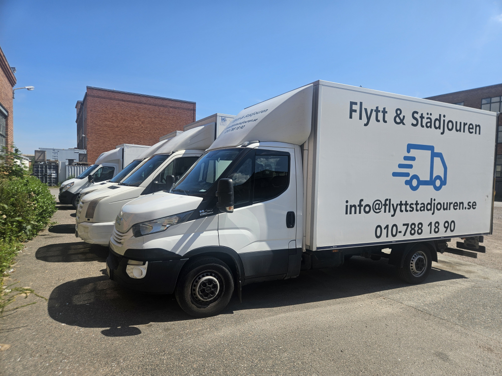 Fyra flyttbilar parkerade i linje på en stor gårdsplan.